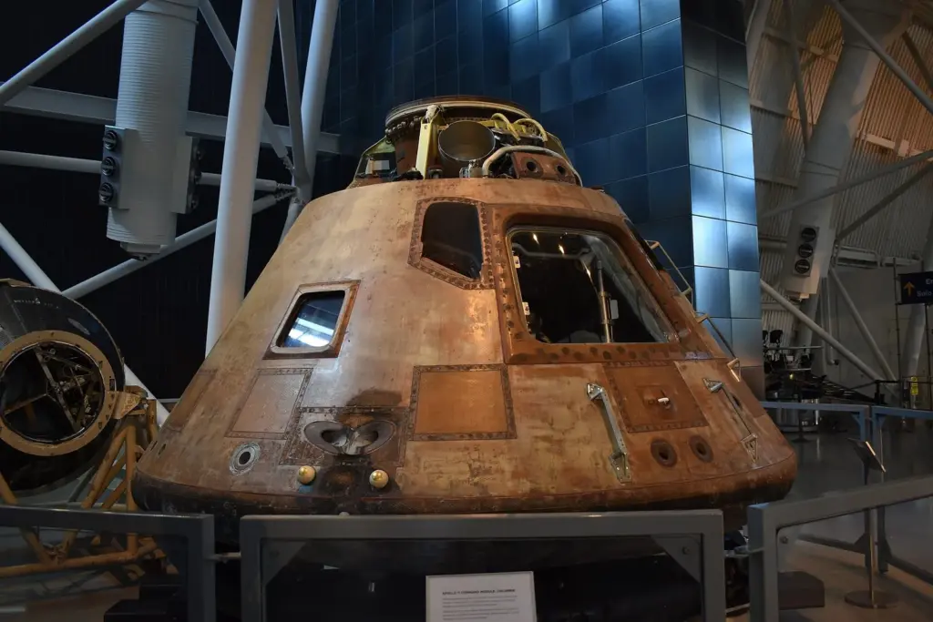 The scorched, cone-shaped Apollo 11 command module Columbia on a display stand in a large hangar