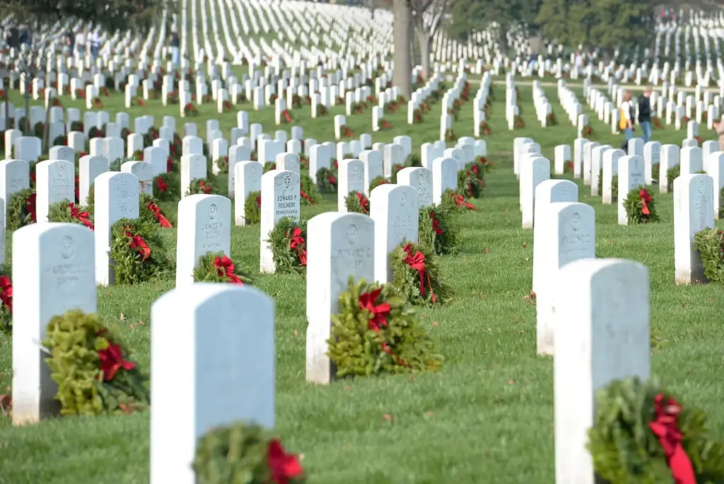 Evergreen wreaths with red bows laid at rows of white headstones