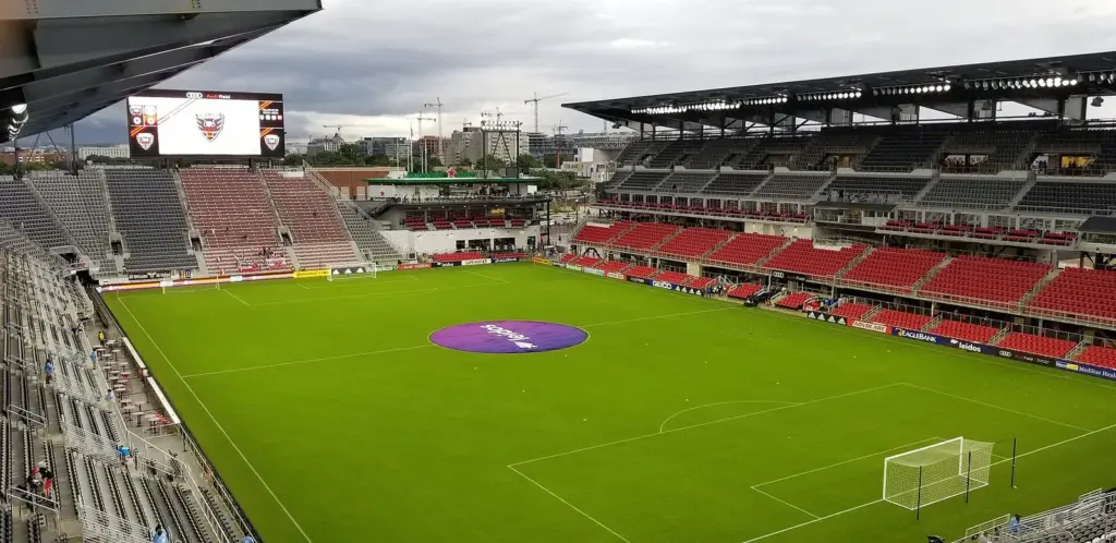 The red seats and green field inside Audi Field at Buzzard Point, with the upper deck and video board