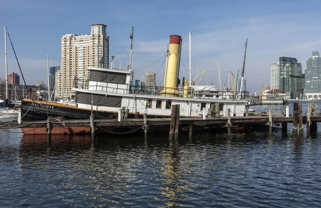 A historic tugboat moored at a pier in Baltimore's Inner Harbor with city towers behind