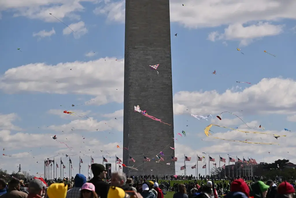 Dozens of kites flying around the Washington Monument above a crowd during the Blossom Kite Festival