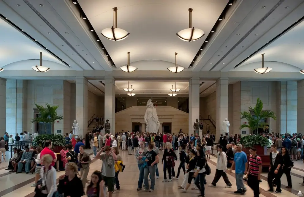 Visitors crossing the long, skylit Emancipation Hall in the Capitol Visitor Center, lined with statues