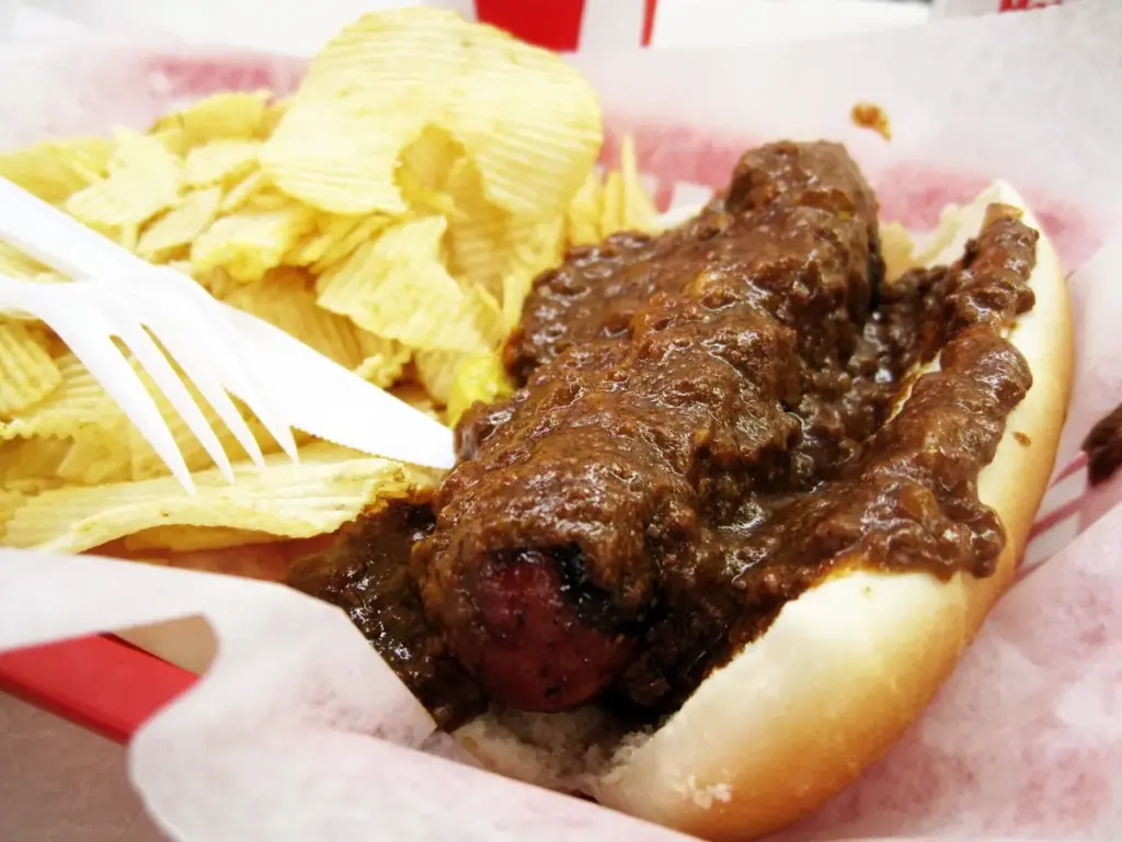 A chili-covered half-smoke sausage in a bun with potato chips in a paper-lined basket