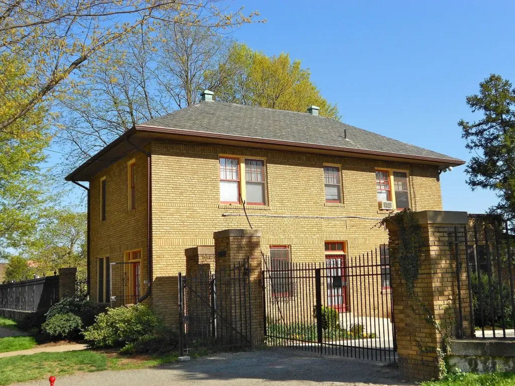 The yellow-brick gatehouse and iron gate of Congressional Cemetery under spring trees