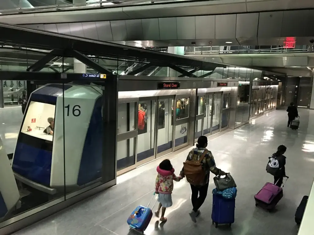 Travelers with rolling suitcases walking toward an AeroTrain at an underground Dulles station