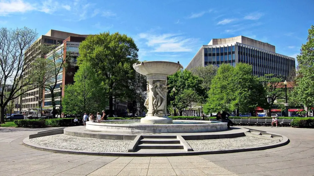 The white marble fountain at the center of Dupont Circle surrounded by trees, benches and office buildings