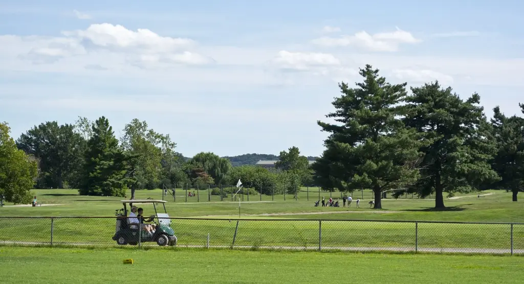 Golfers in a cart on the tree-lined fairways of East Potomac Golf Course on a summer day