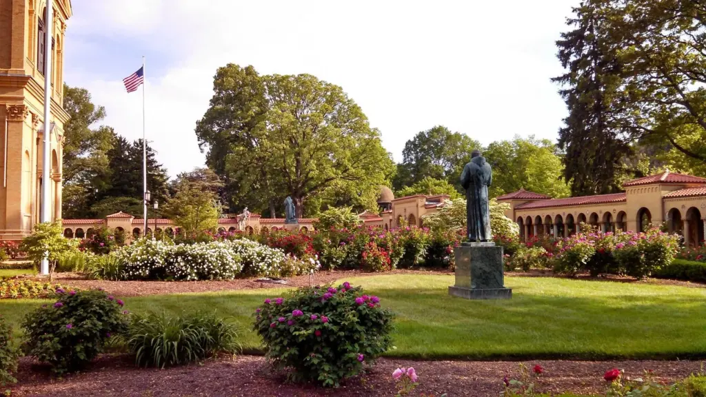Rose beds and a bronze statue in the gardens of the Franciscan Monastery with its arcaded cloister behind