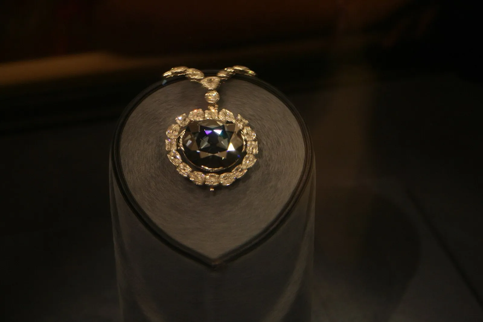 The Hope Diamond, a deep blue stone ringed by white diamonds, on its gray pedestal in a darkened display case
