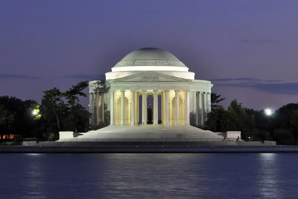 The Thomas Jefferson Memorial lit up at dusk, reflected in the calm water of the Tidal Basin