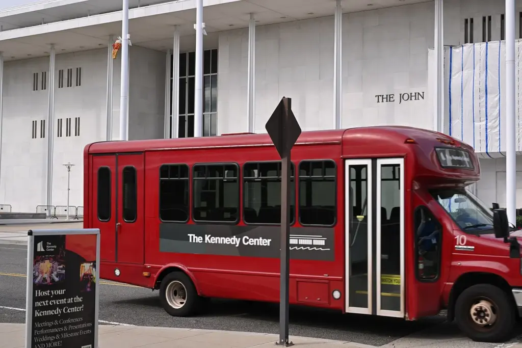 A red Kennedy Center shuttle bus parked outside the center's white marble facade