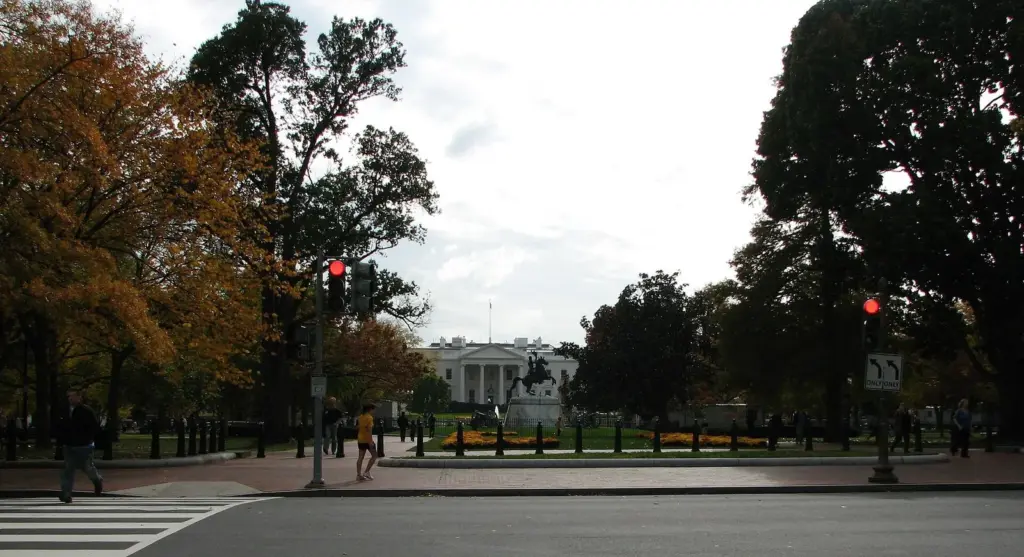 Lafayette Park's trees and lawn framing a distant view of the White House North Portico across Pennsylvania Avenue