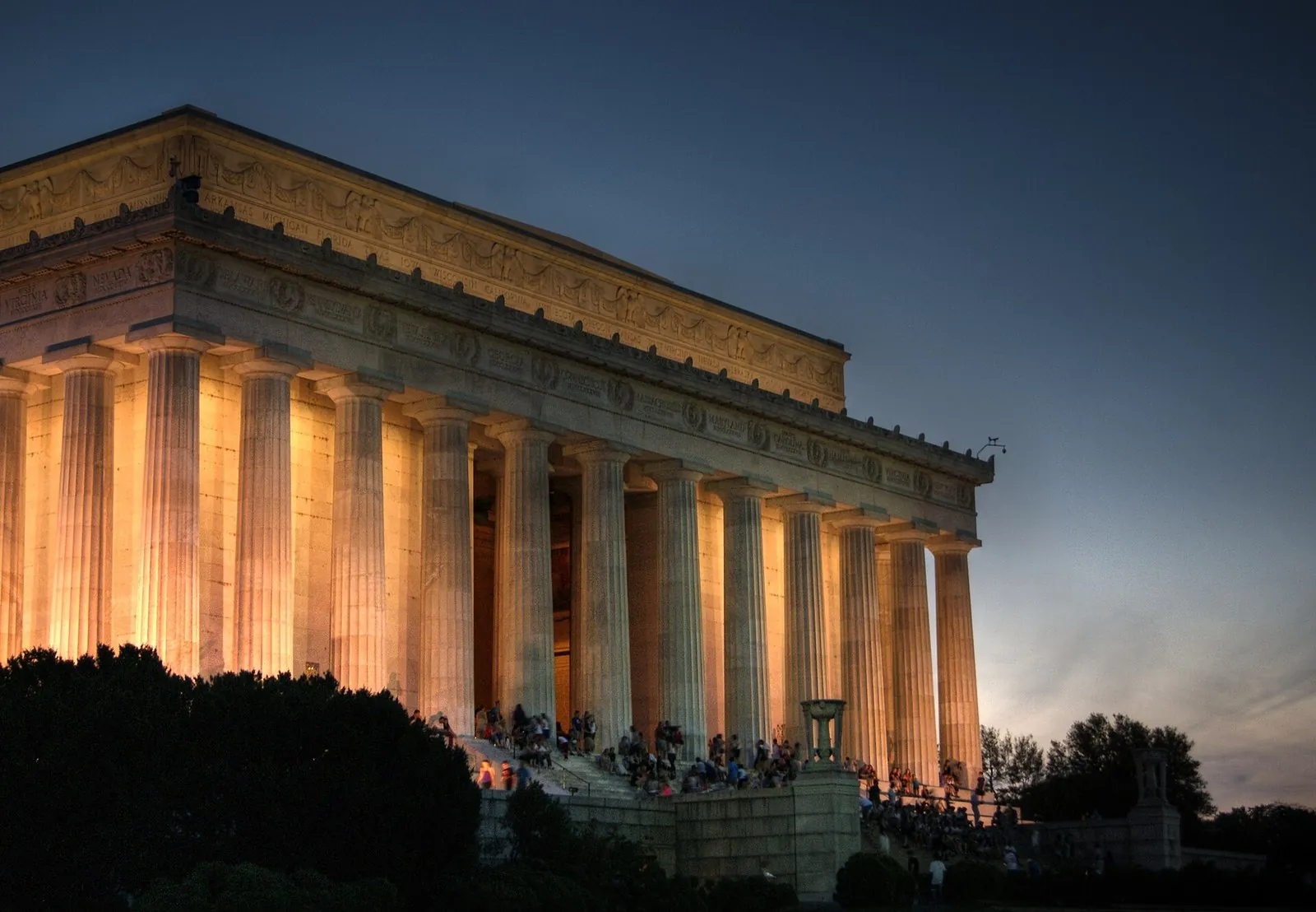 The Lincoln Memorial's colonnade lit gold in the evening, with visitors gathered on the steps