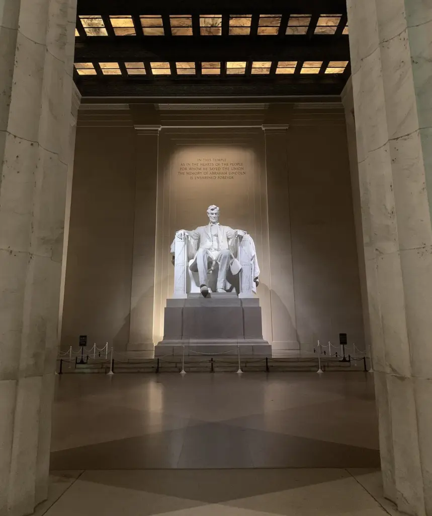 The seated marble statue of Abraham Lincoln inside the Lincoln Memorial, lit from above between tall columns