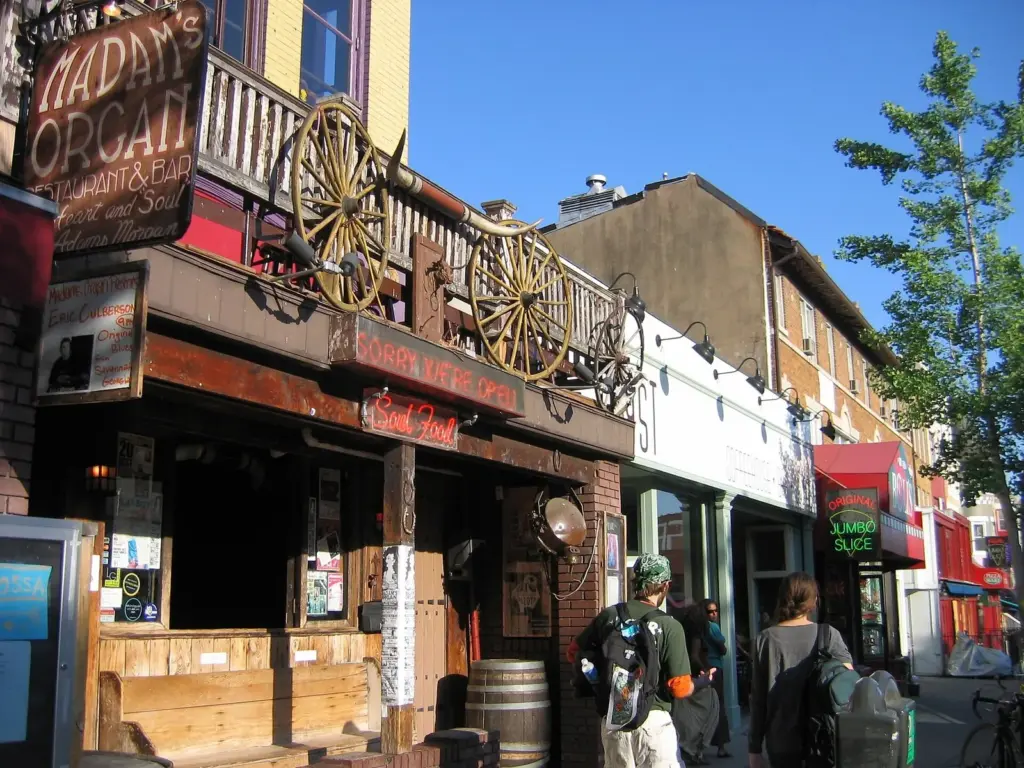 The carved wooden front of Madam's Organ bar on 18th Street in Adams Morgan, with a jumbo slice sign next door