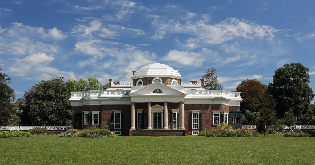 Monticello's domed brick house with white portico behind a broad lawn under a blue sky