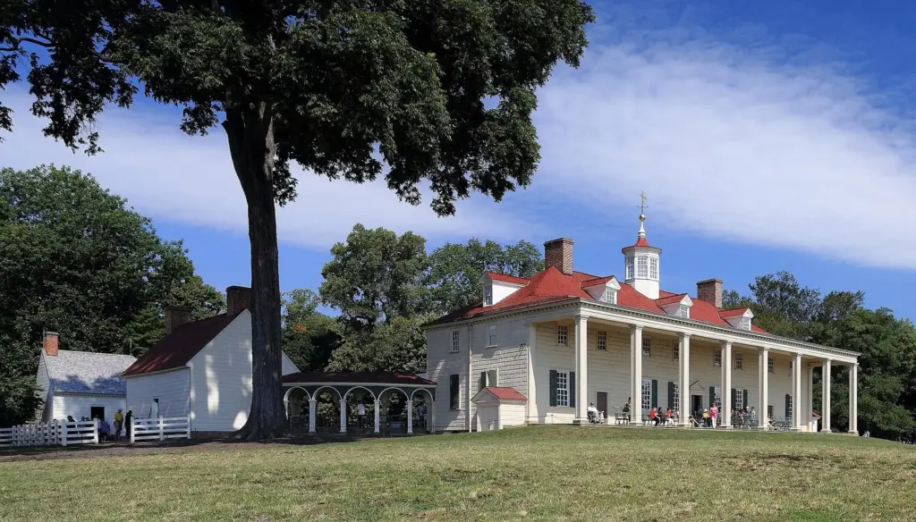 The white-columned piazza and red roof of George Washington's Mount Vernon mansion on a lawn under a large tree