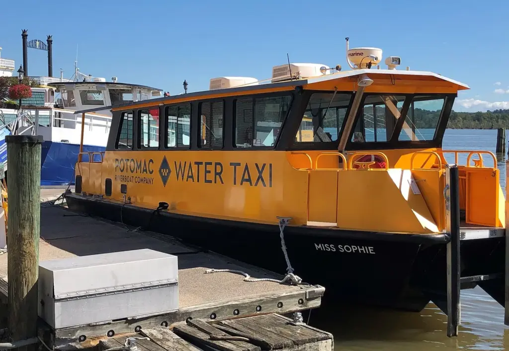 An orange Potomac Water Taxi boat moored at the Alexandria waterfront