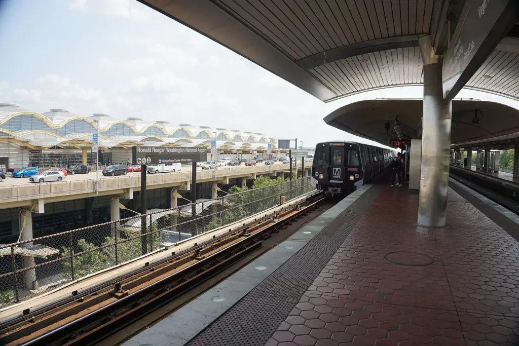 A Metro train at the elevated Reagan National Airport station, with the terminal's domed roofs beside the platform