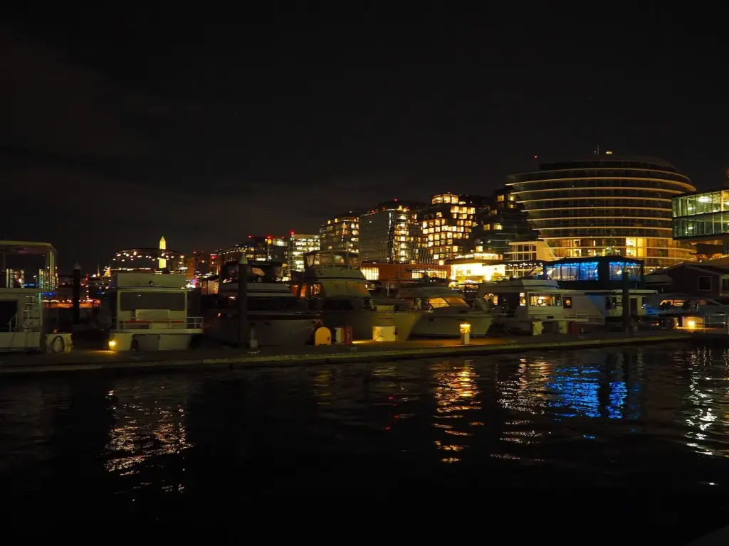 Lit restaurants, apartments and boats along the Wharf waterfront at night, reflected in the Washington Channel
