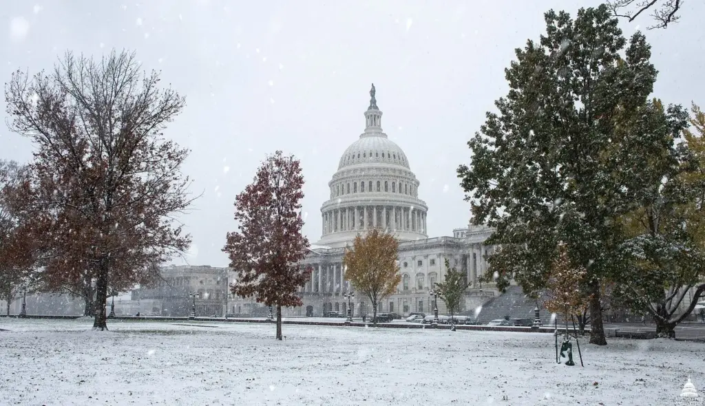 The U.S. Capitol dome behind snow-covered lawns and trees still holding orange autumn leaves