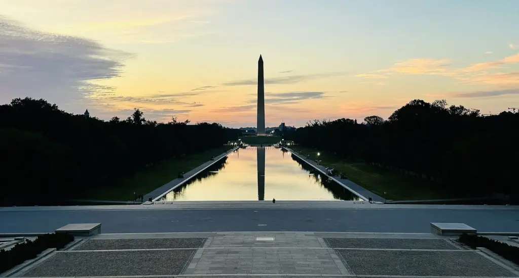 The Washington Monument reflected in the long Reflecting Pool under a pink and gold sunrise sky